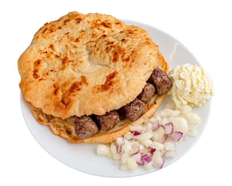 Chevapi in golden lepinja bread, with kajmak and chopped onion on a white plate